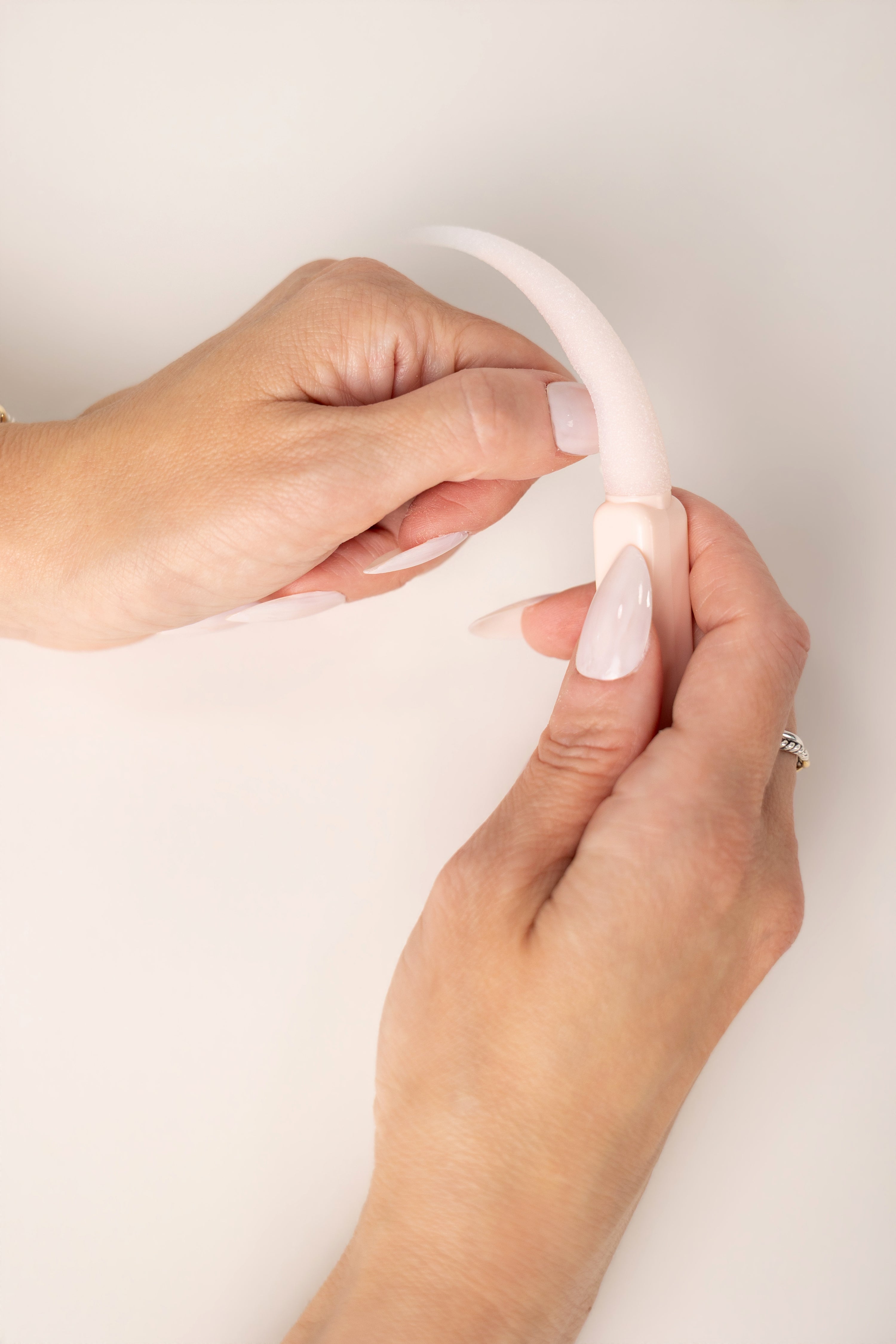 Close-up of hands holding a light pink buffie against a light background