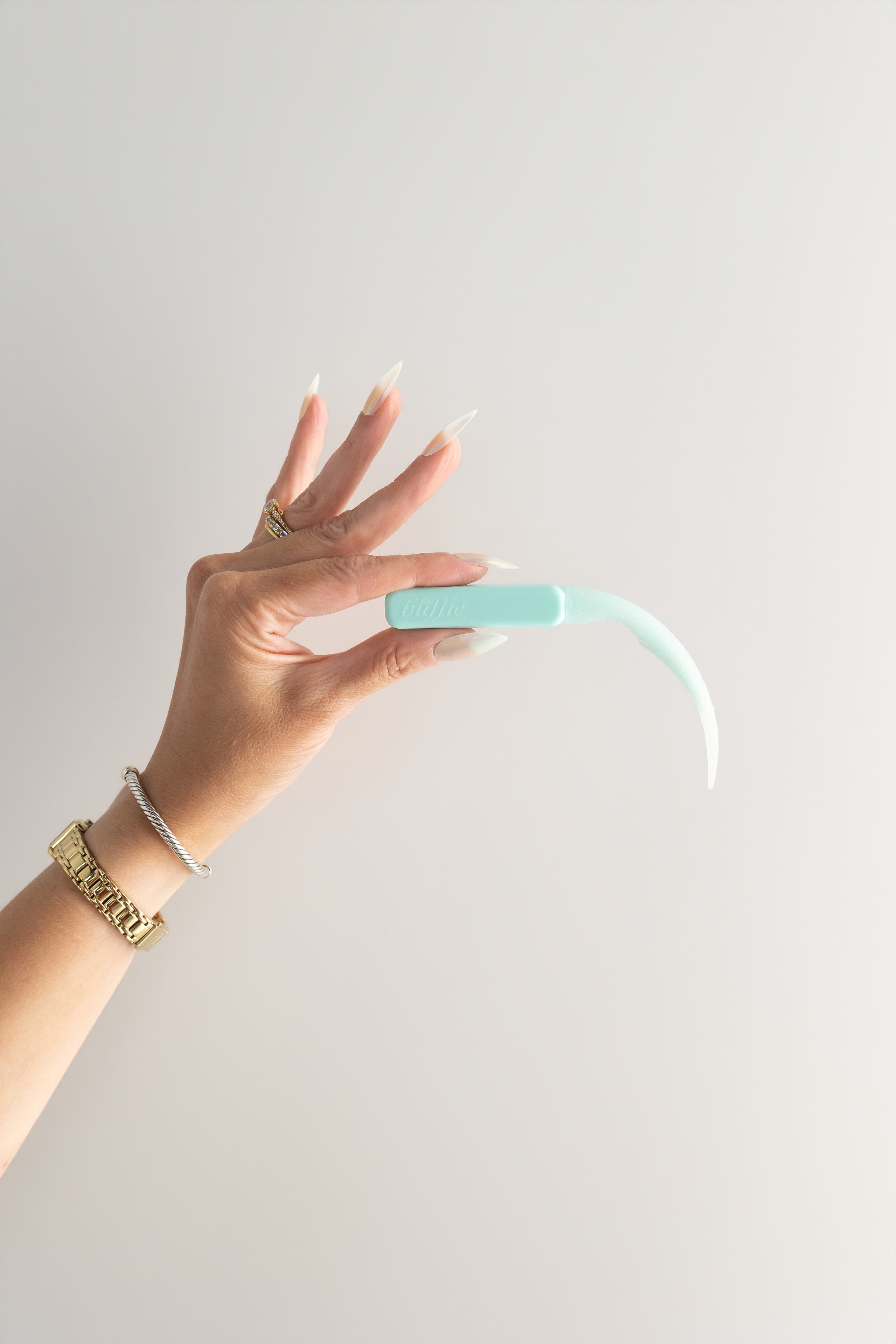 Hand holding a light green curved buffing tool against a plain background