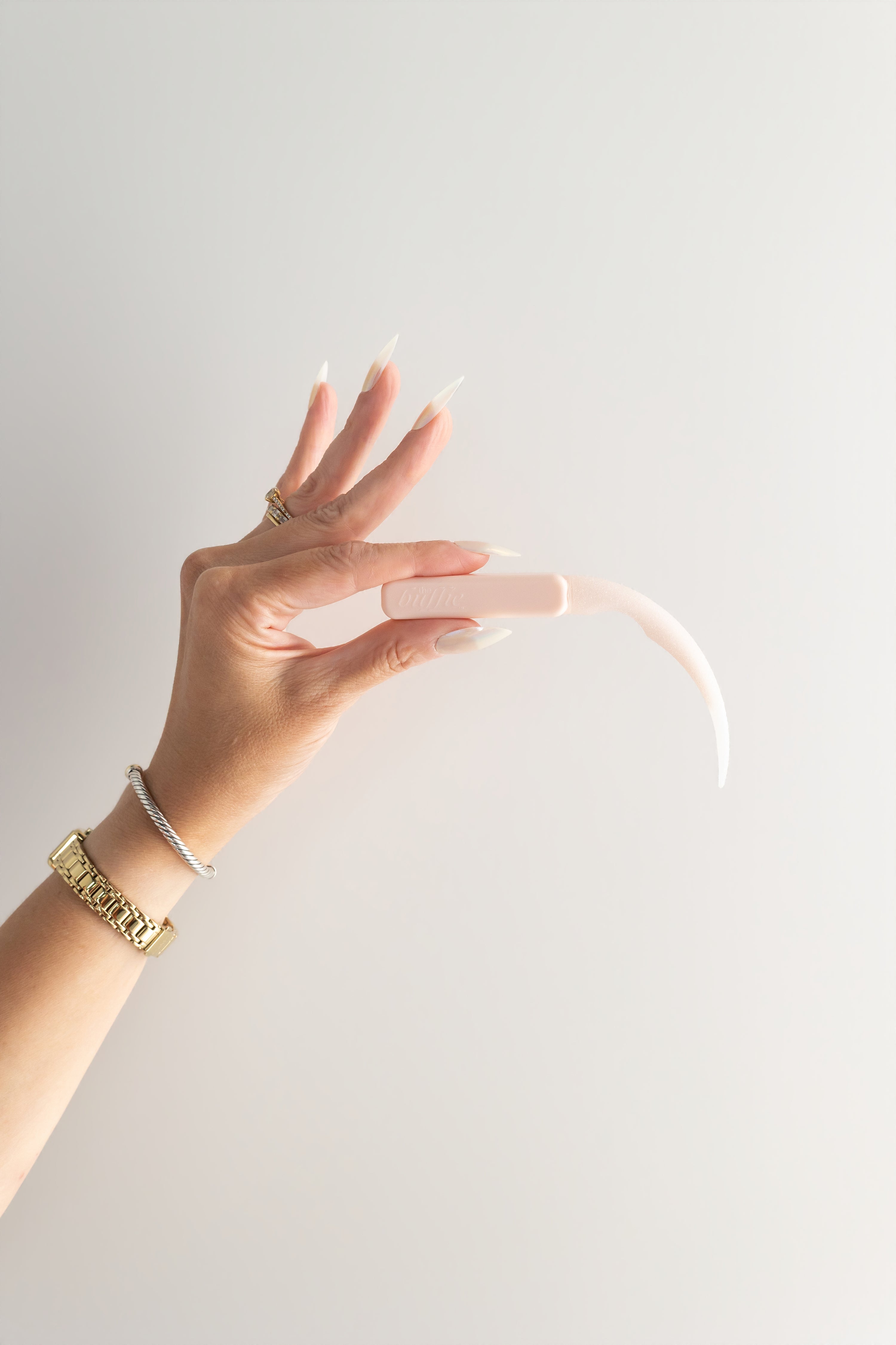 Hand holding a pastel pink buffie with a hand wearing white press ons against a light background