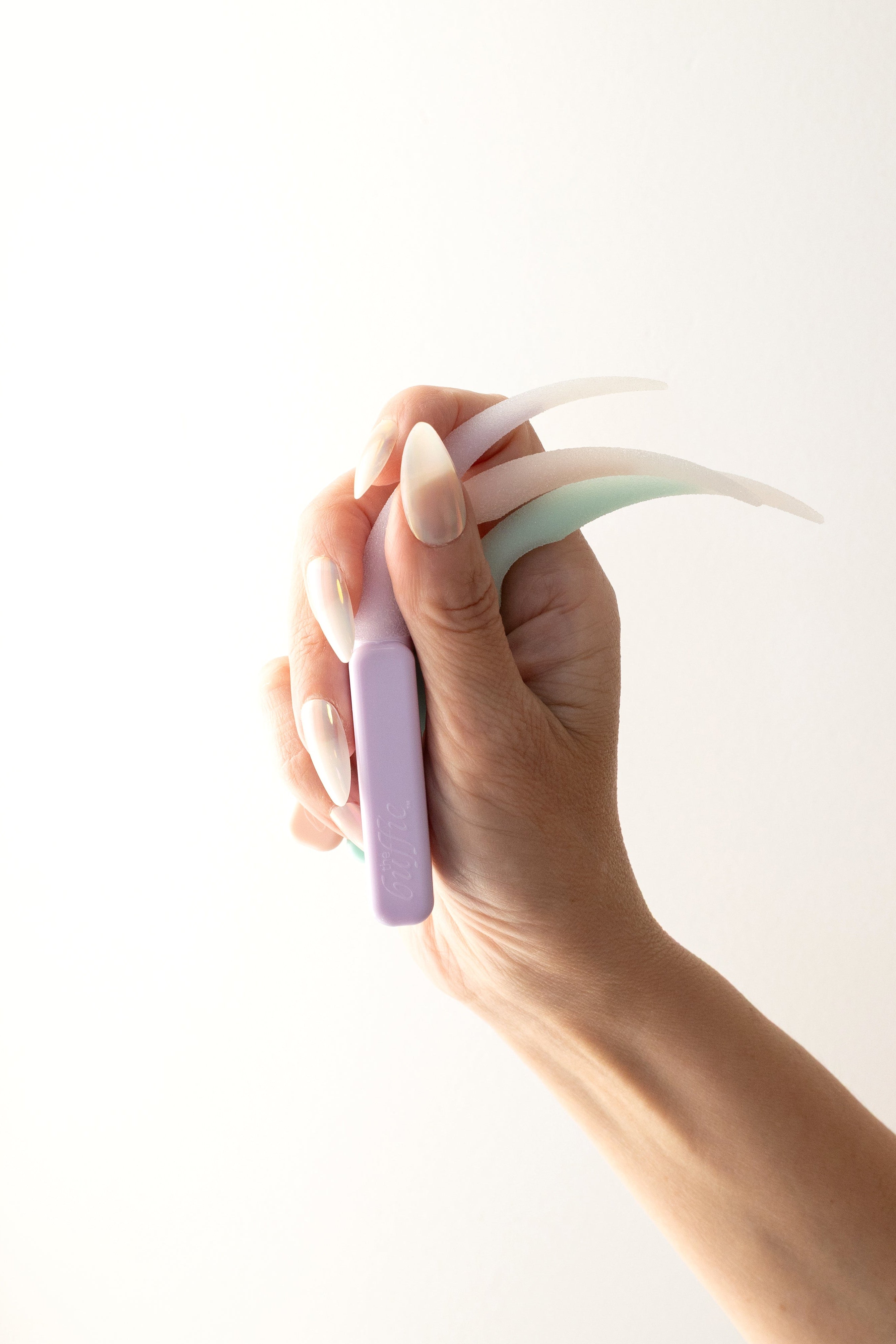 Hand holding three pastel colored nail buffing tools against a white background