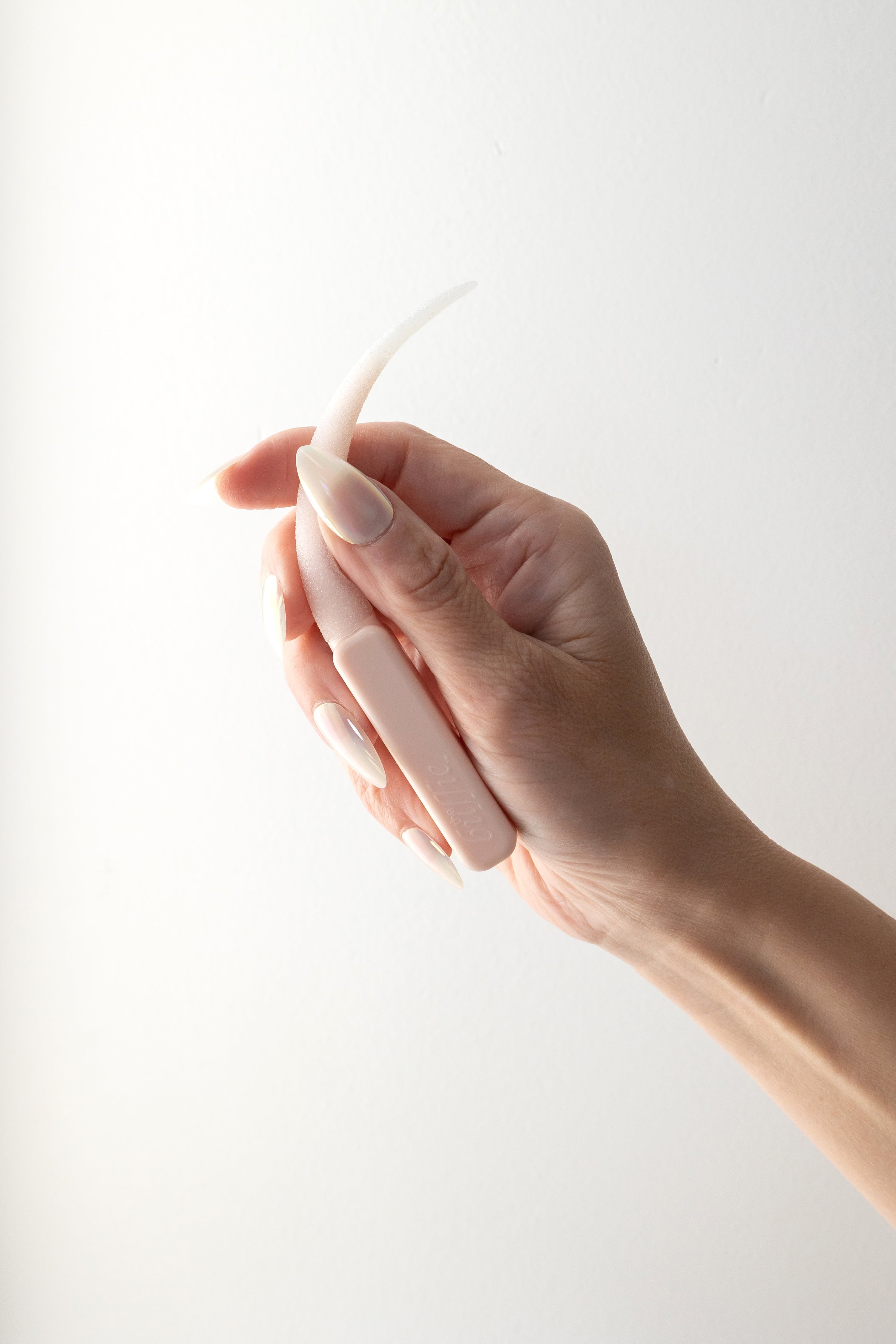 Hand holding a pastel pink buffie against a light background