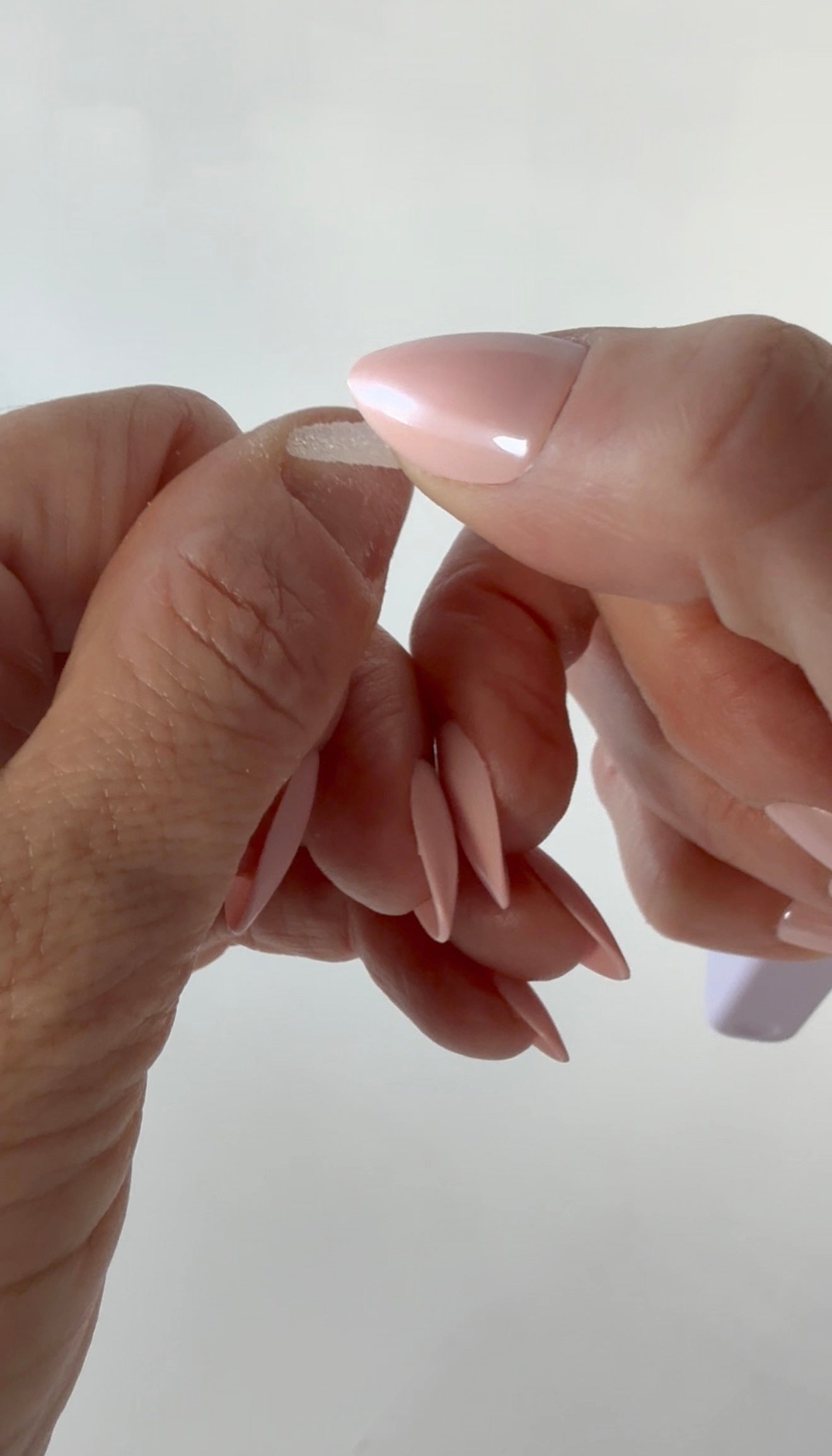 Close-up of using tool tip to buff cuticles with pointed nails against a plain background